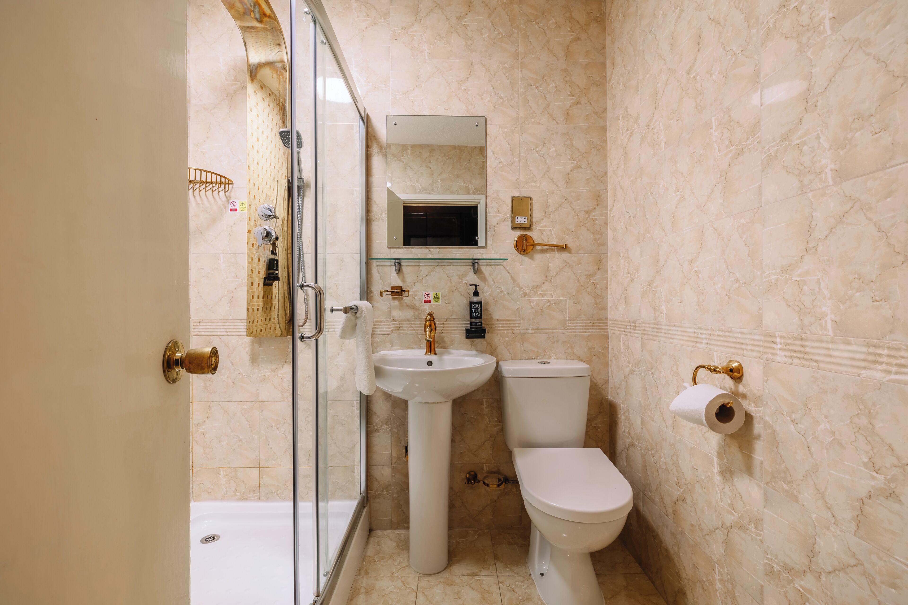 A bathroom with a glass shower enclosure, a pedestal sink, a toilet, and a small mirror above the sink.