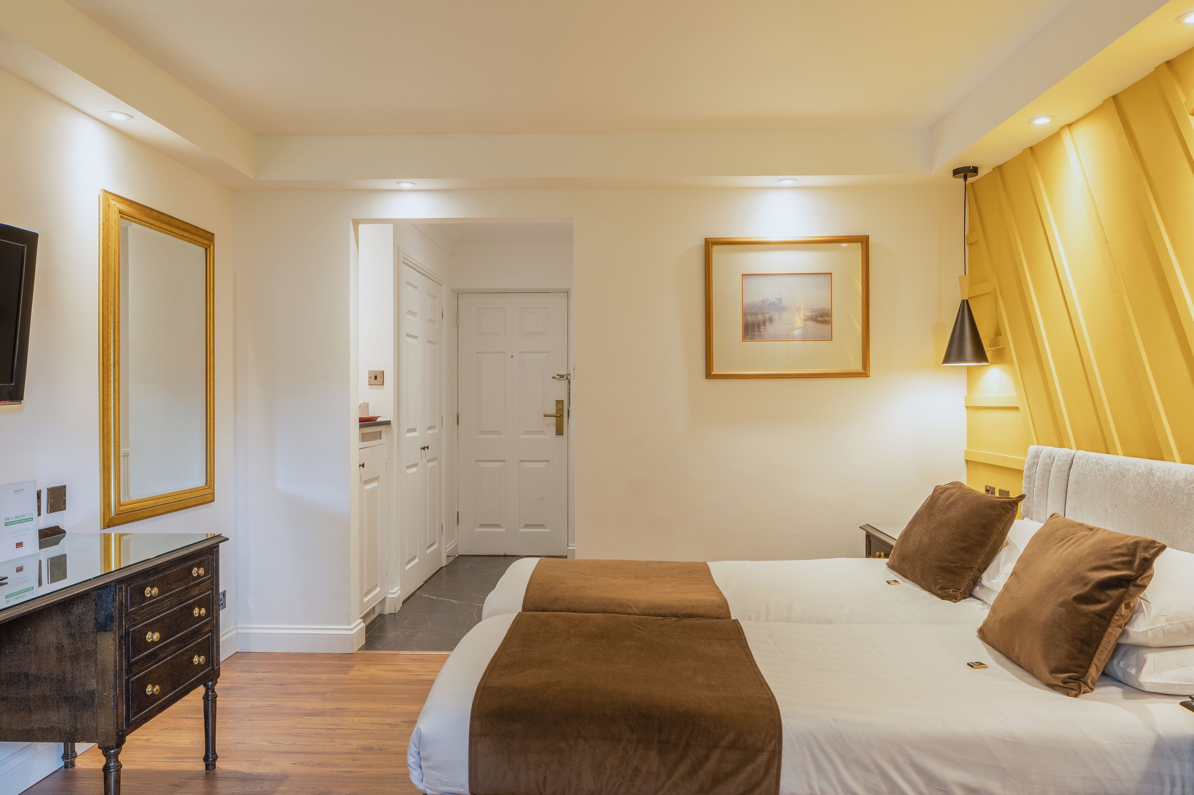 A hotel room with a bed, a dresser, a mirror, a door, and a framed picture on the wall.