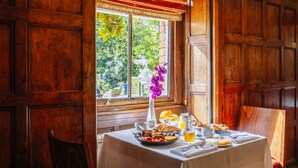 A breakfast table with a white tablecloth, a vase with flowers, and a window with a view of greenery. - Muthu Belstead Brook Hotel (Ipswich)
