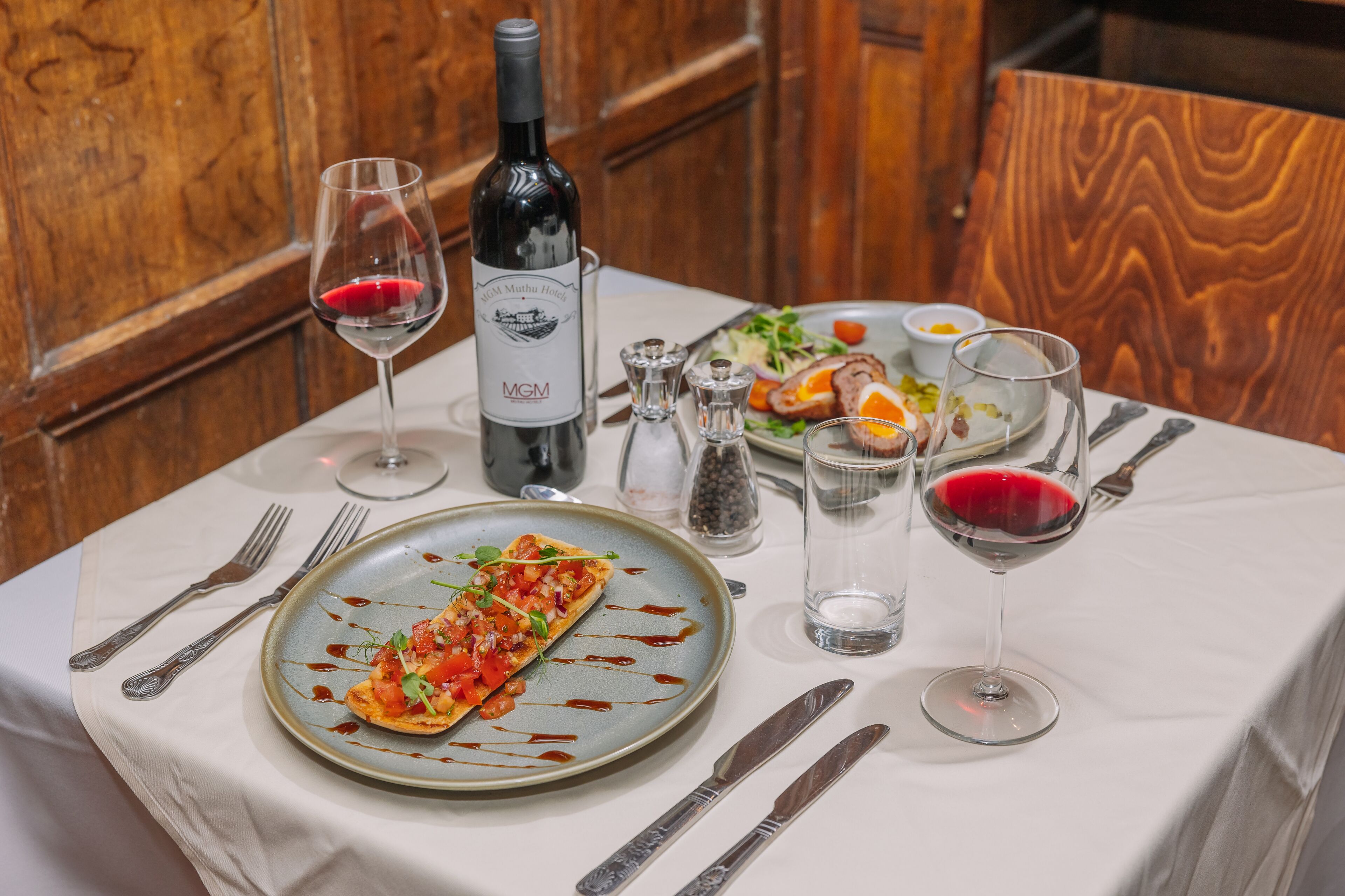 Una mesa de comedor con un plato de comida, una botella de vino y copas.