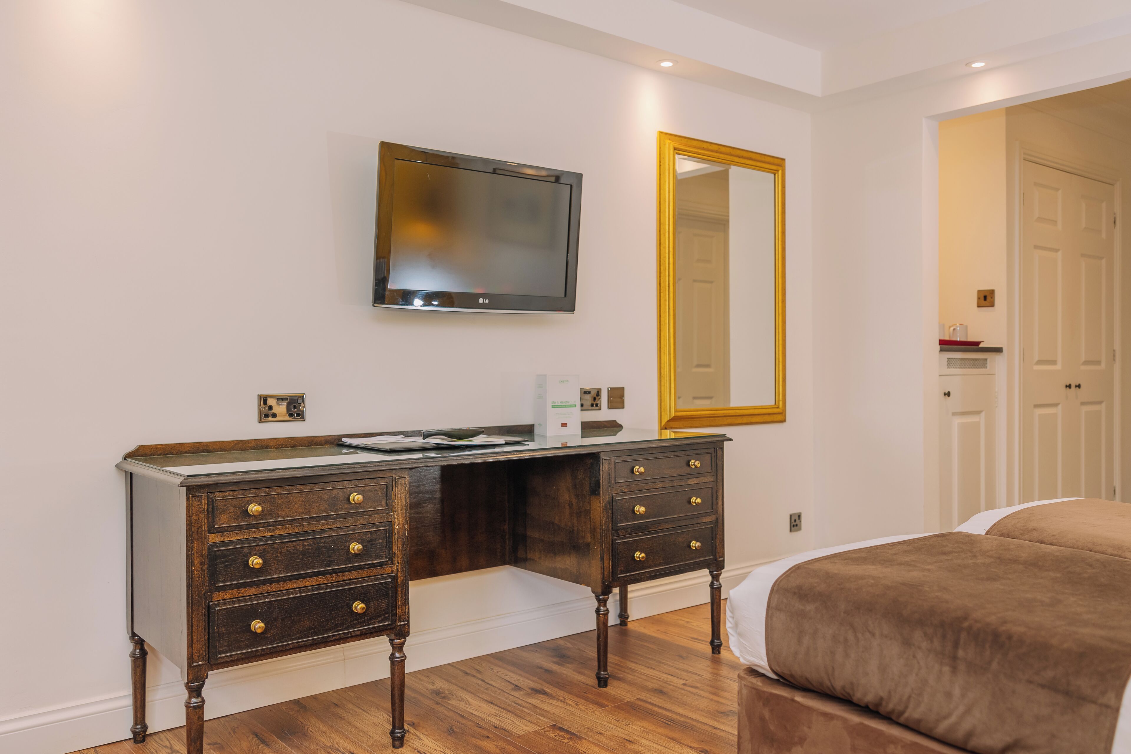 A bedroom with a bed, a dresser with drawers, a flat-screen TV, and a large mirror.