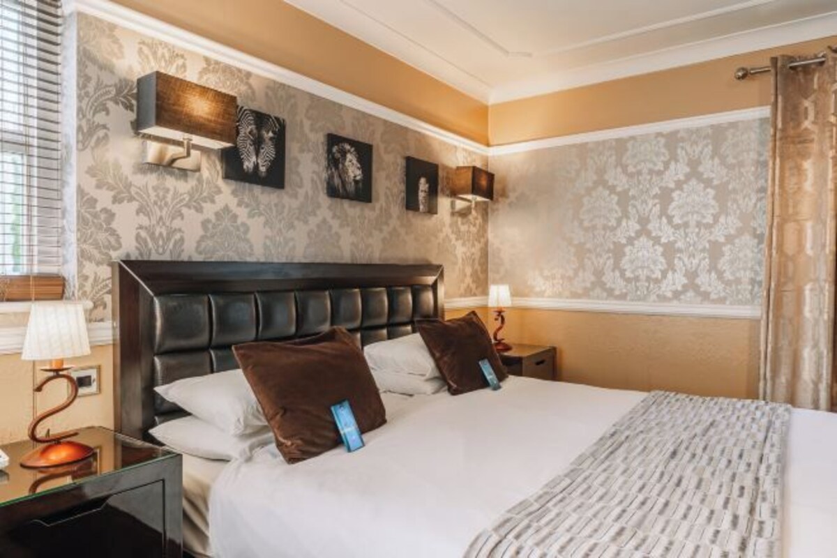 Ein Hotelzimmer mit einem großen Bett, zwei Nachttischen, einer Kopfteil und Wandlampen.