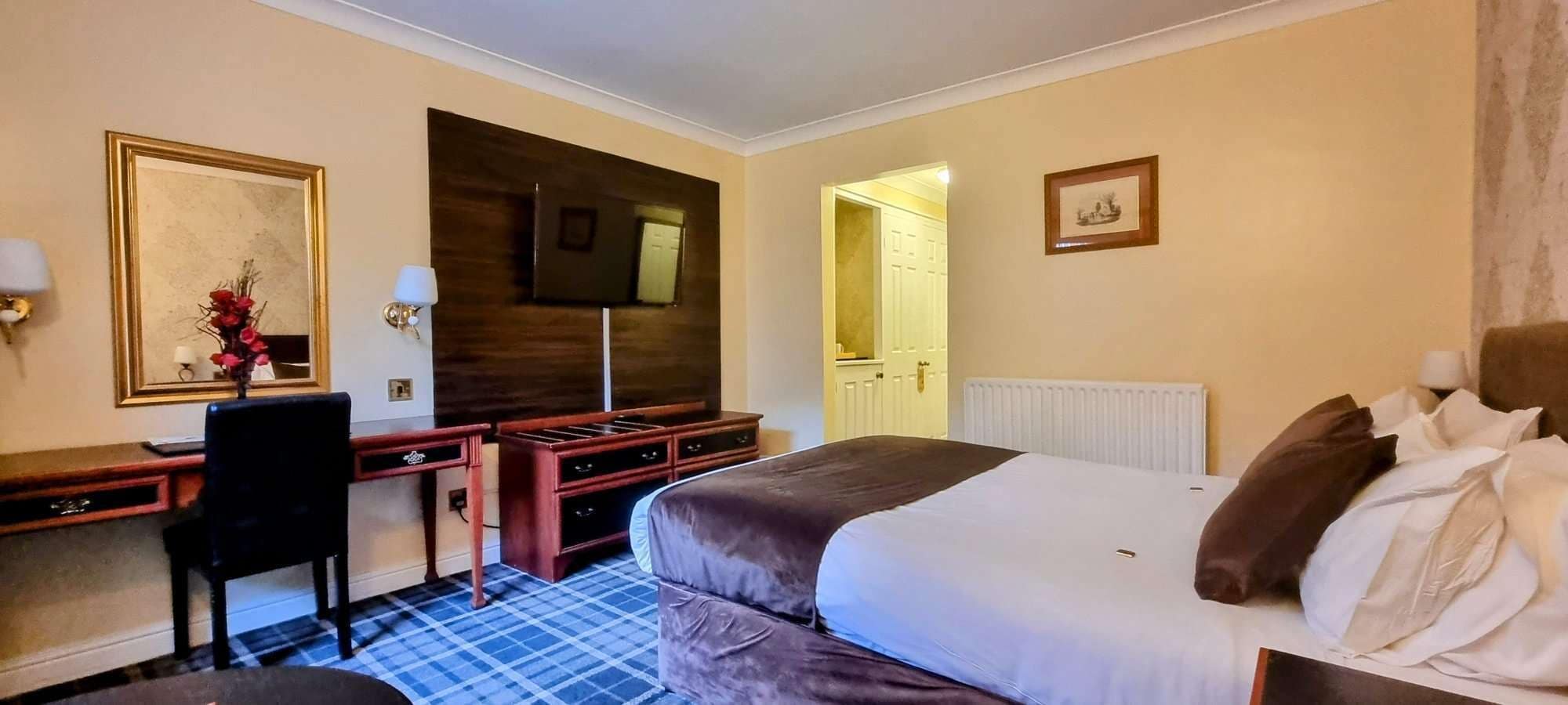 Una habitación de hotel con cama, escritorio, silla, televisor y espejo.