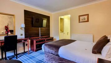 Una habitación de hotel con cama, escritorio, silla, televisor y espejo.