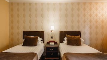 Een hotelkamer met twee bedden, een nachtkastje met een lamp en behang met een patroon.