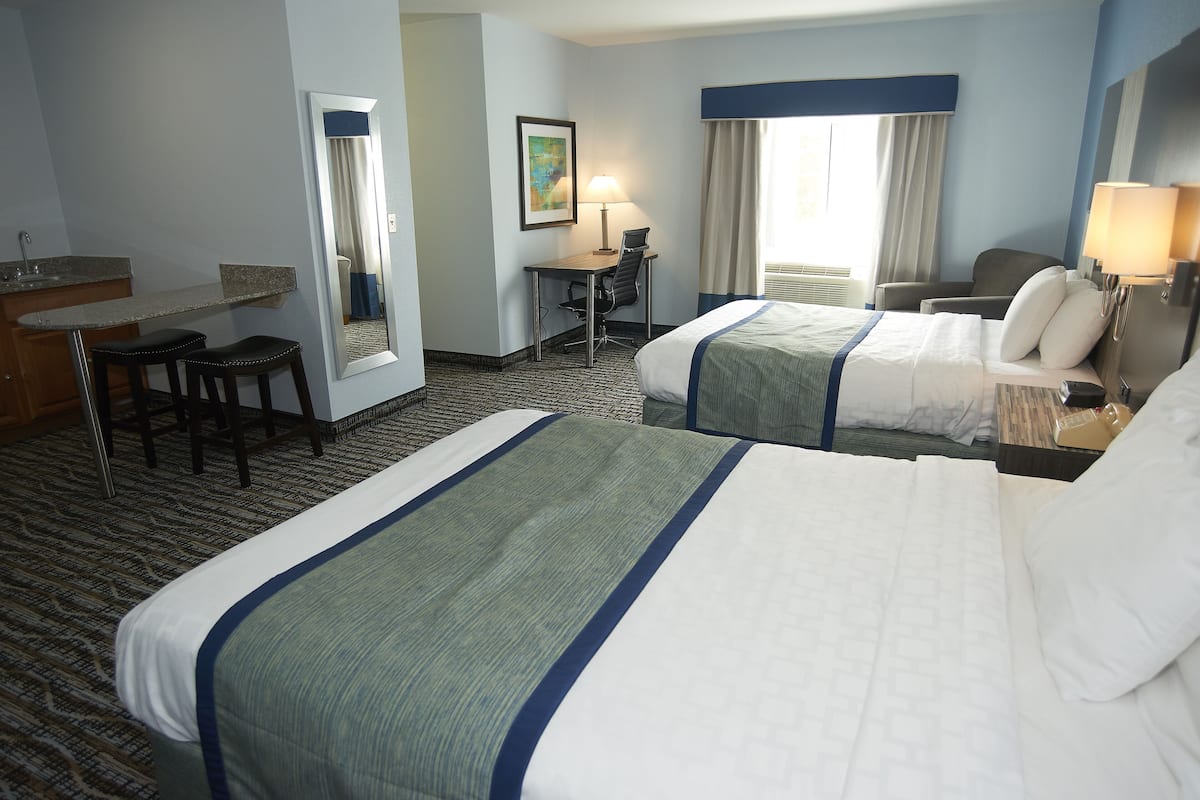 A hotel room with two beds, a desk, a chair, a small bar area, and a bathroom.