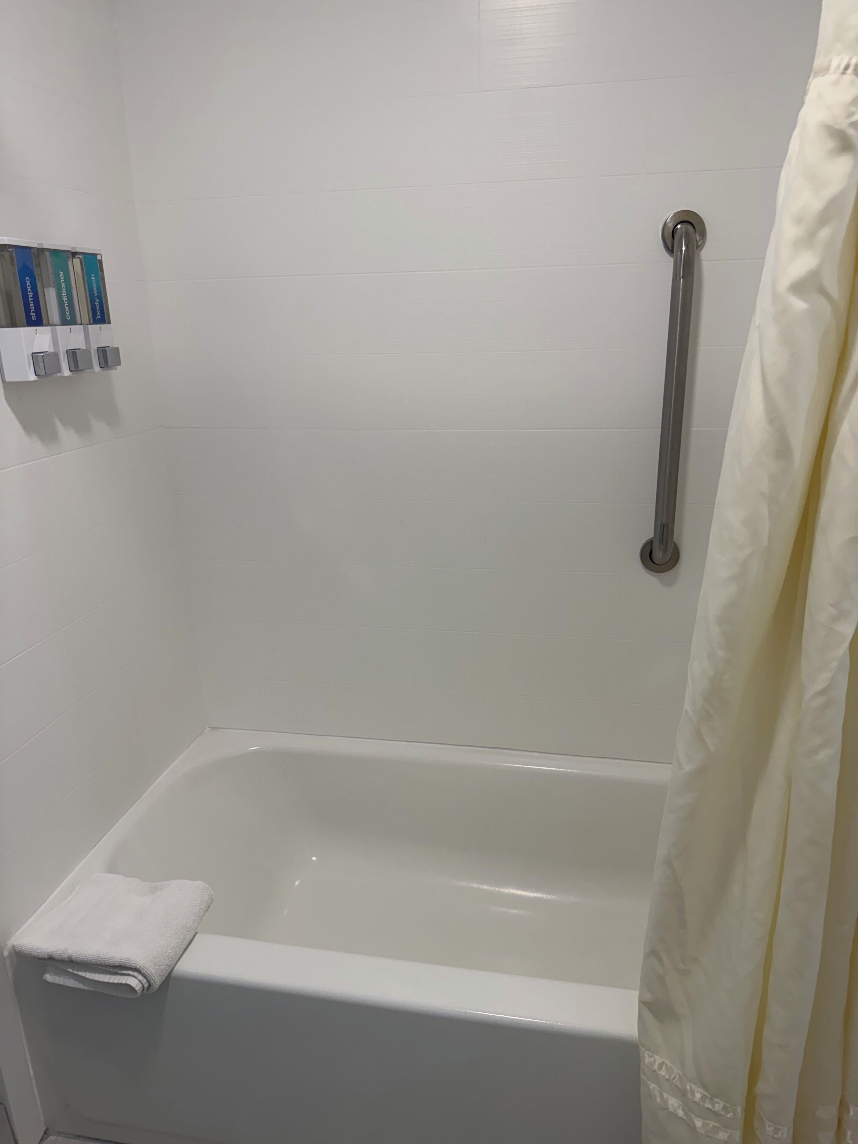 A bathroom with a bathtub, a handrail, and a towel rack with toiletries.