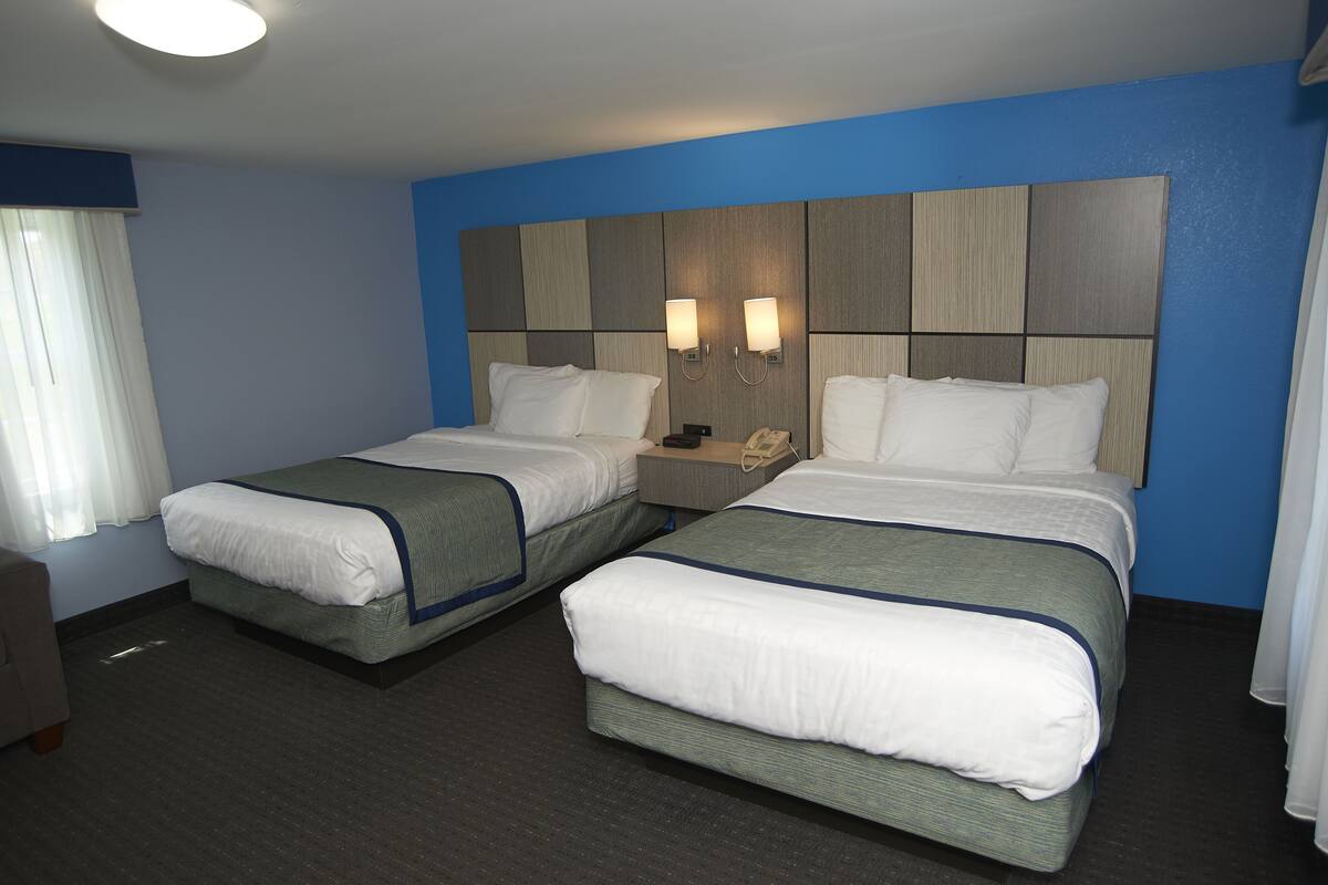 A hotel room with two beds, a nightstand, and a desk with a phone.