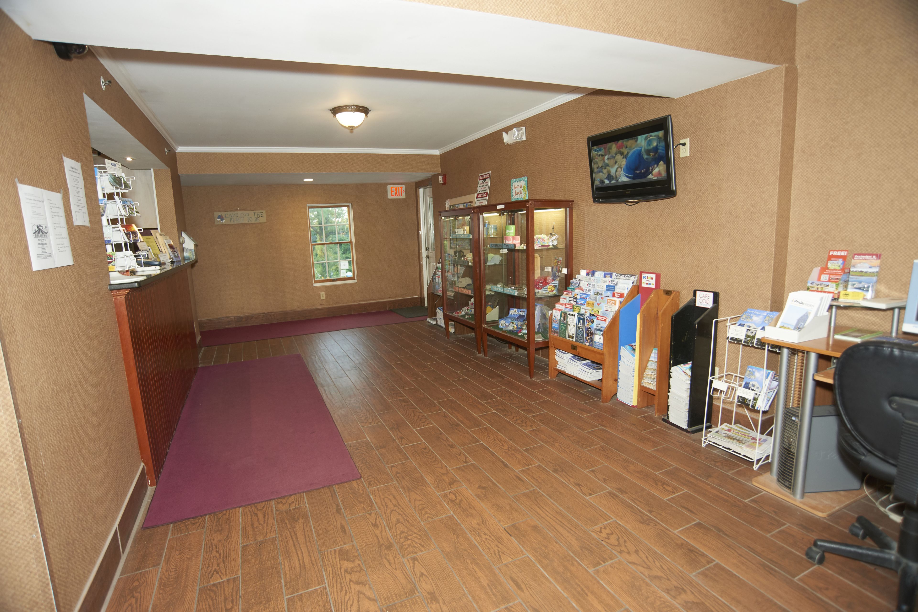 A reception area with a wooden floor, a purple mat, a glass display case, and a television on the wall.