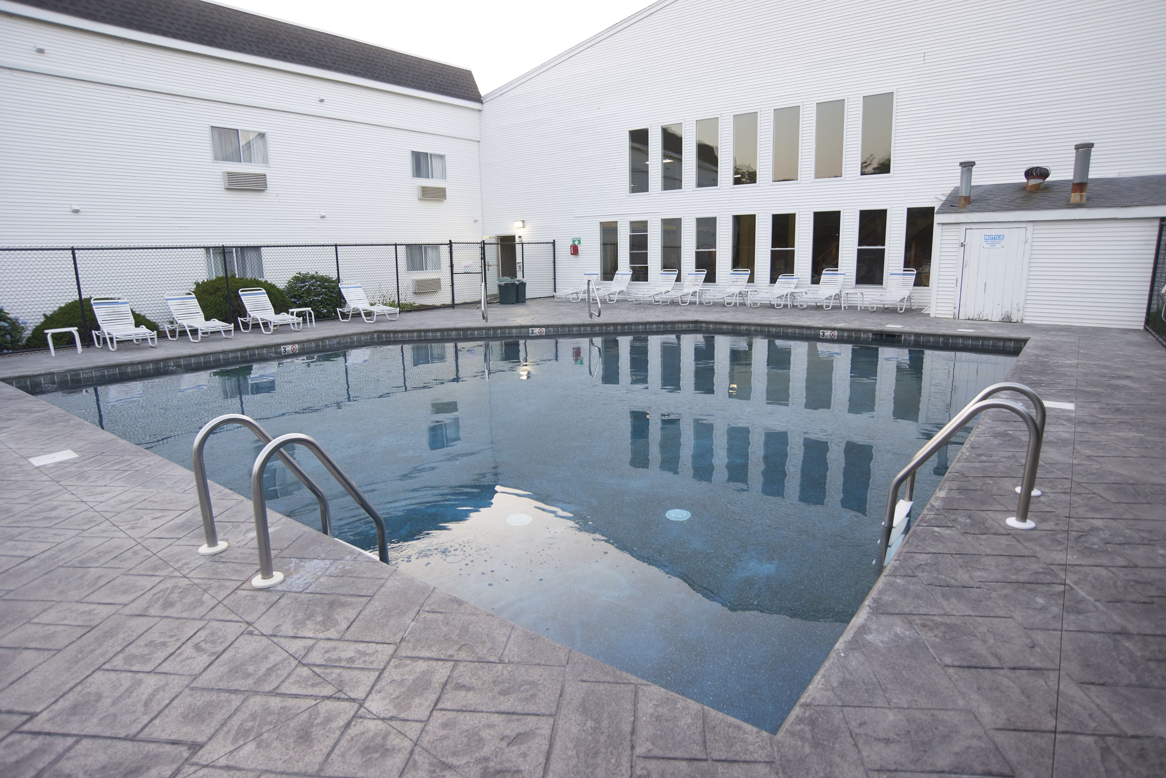 A swimming pool with a tiled deck, lounge chairs, and a white building with large windows.