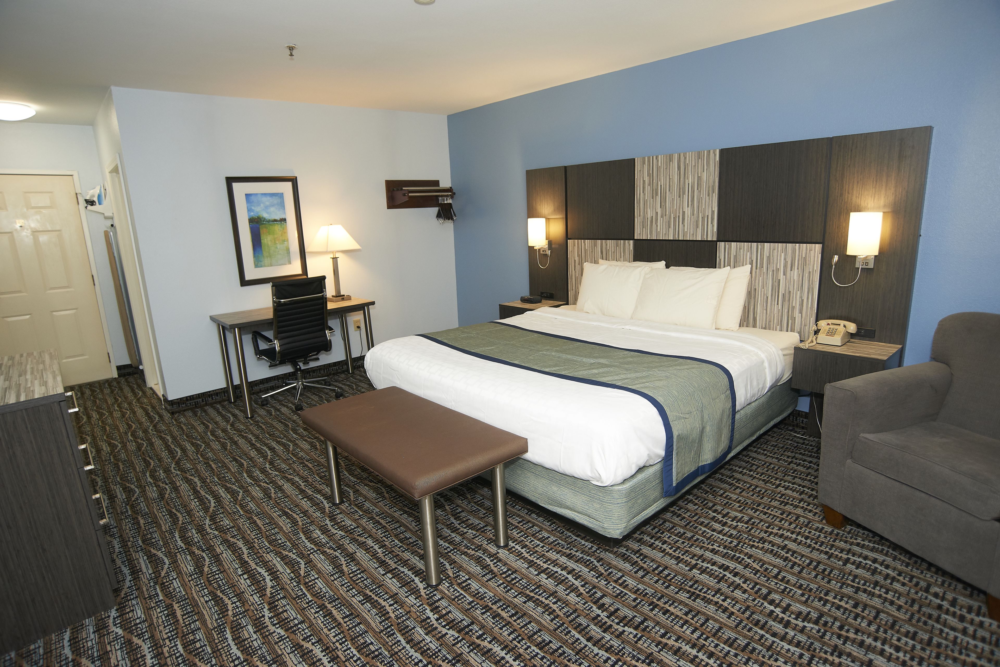 Een hotelkamer met een bed, een bureau, een stoel en een bankje.