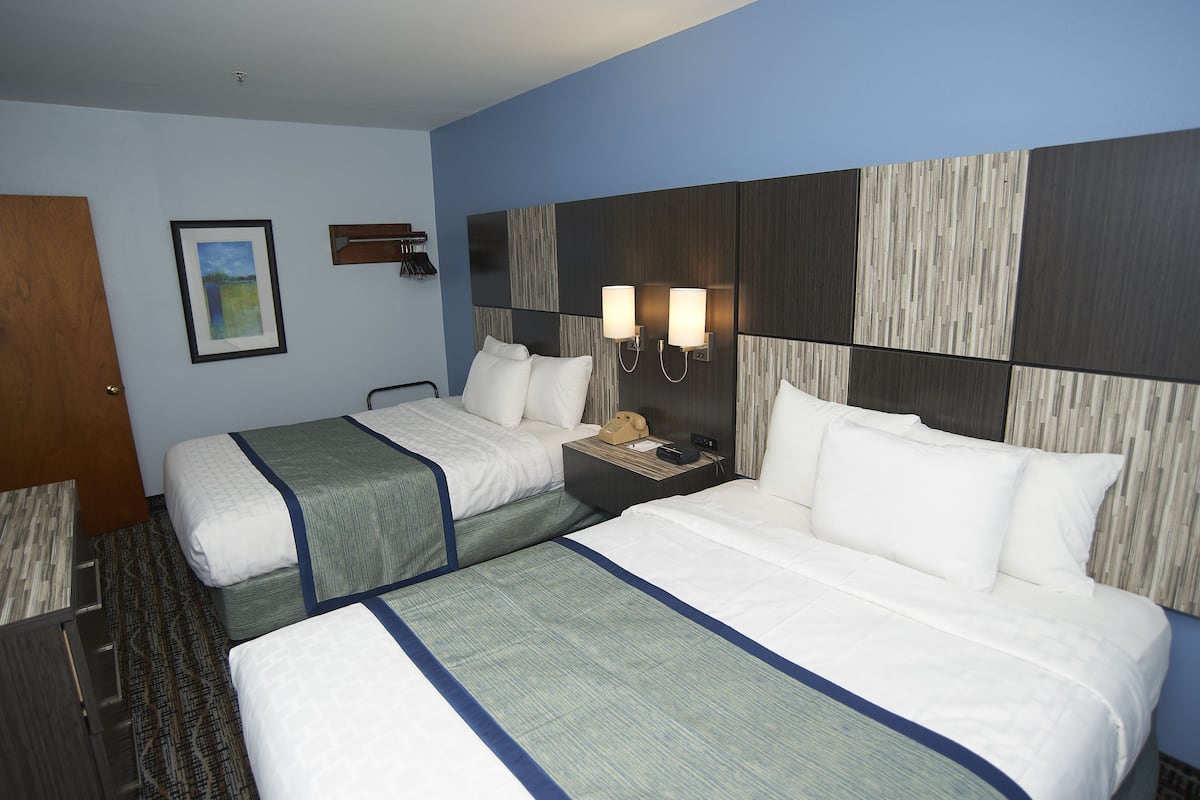 A hotel room with two beds, a nightstand, a framed picture, and a headboard with a textured design.