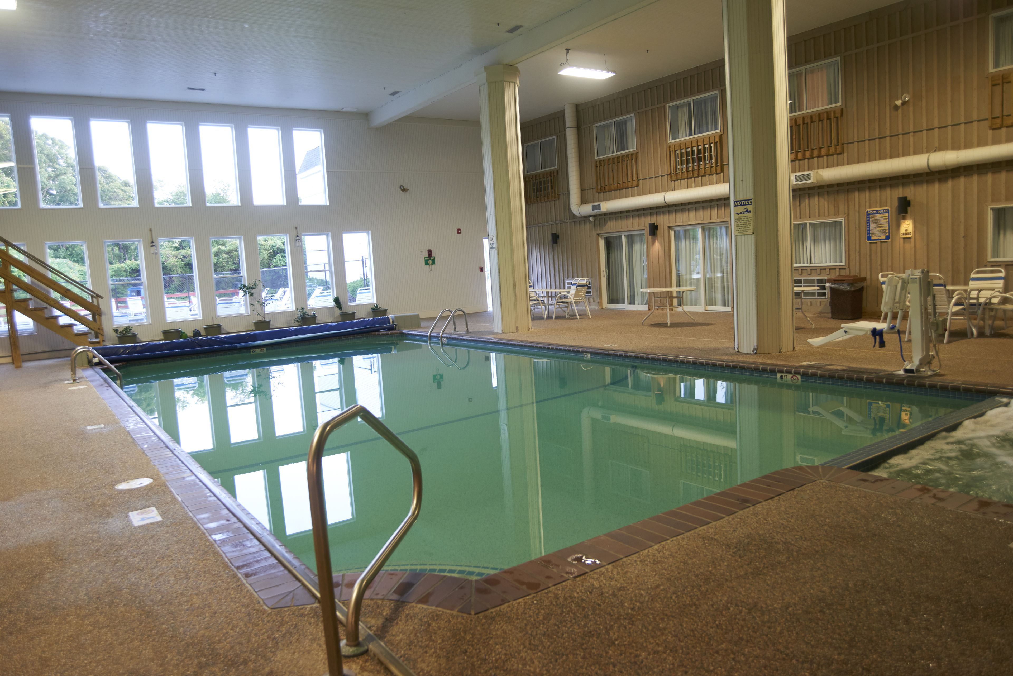Una piscina interior con ventanales amplios, una escalera de piscina y una zona de estar con sillones.
