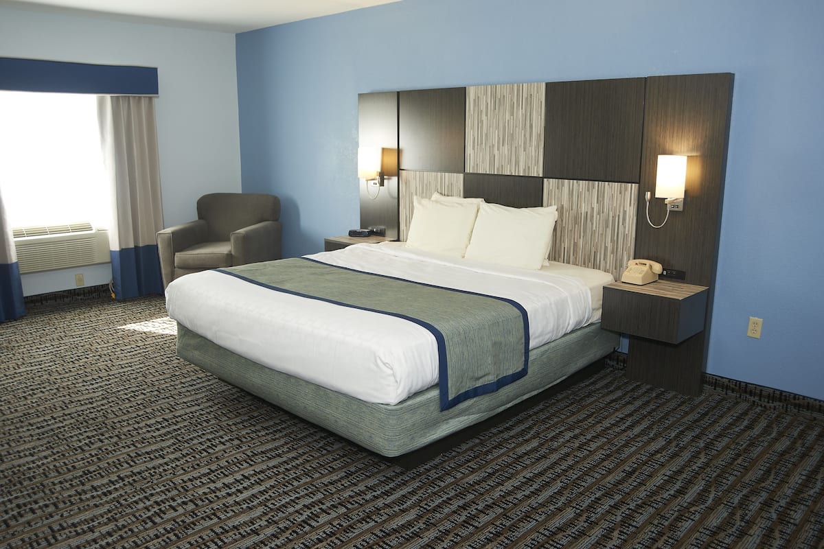 A hotel room with a large bed, a chair, a nightstand with a phone, and a wall-mounted lamp.