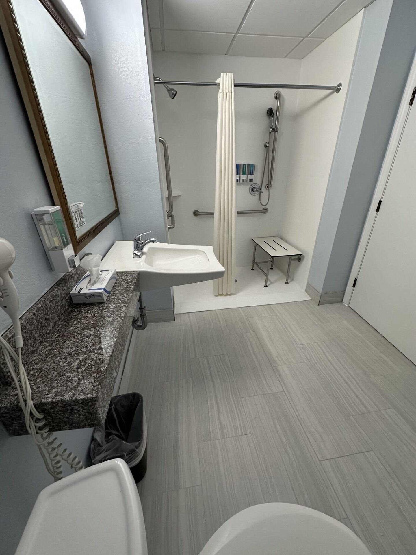 A modern bathroom with a granite countertop, a white sink, a mirror, a shower with a glass door, and a small vanity table.