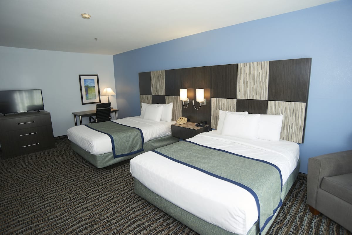 A hotel room with two beds, a desk, a chair, a TV, and a lamp.