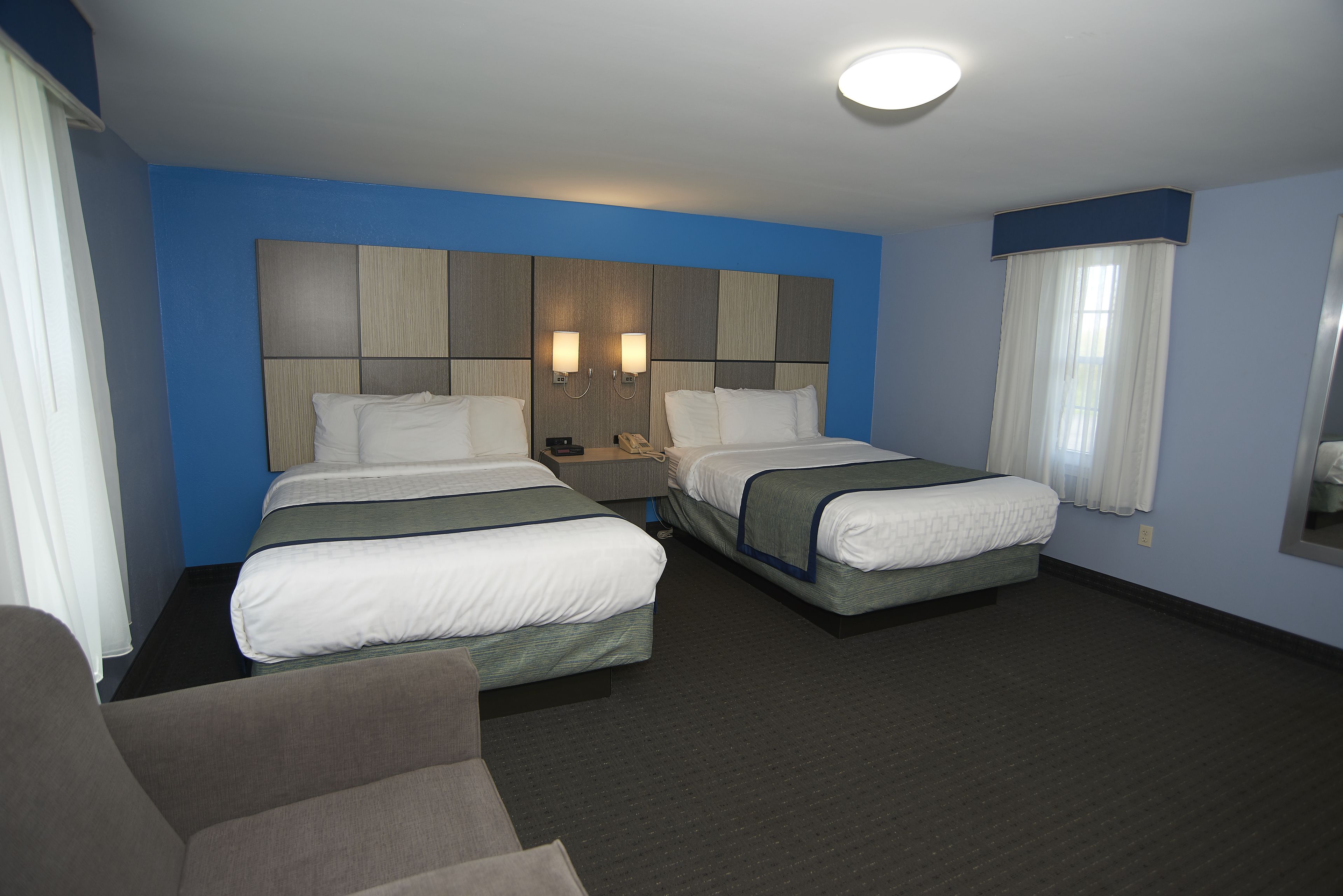 Habitación de hotel con dos camas, una mesita de noche, una silla y una ventana con cortinas.
