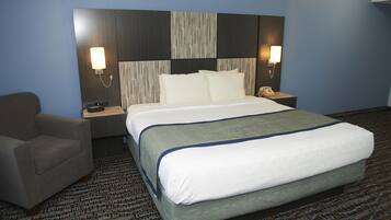 Una habitación de hotel con una cama grande, una silla, una mesita de noche con un teléfono y lámparas fijadas a la pared.