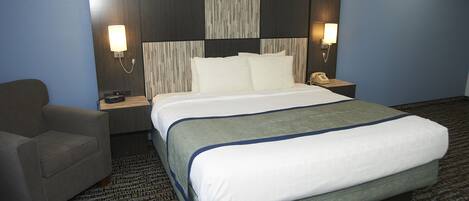A hotel room with a large bed, a chair, a nightstand with a phone, and wall-mounted lamps.