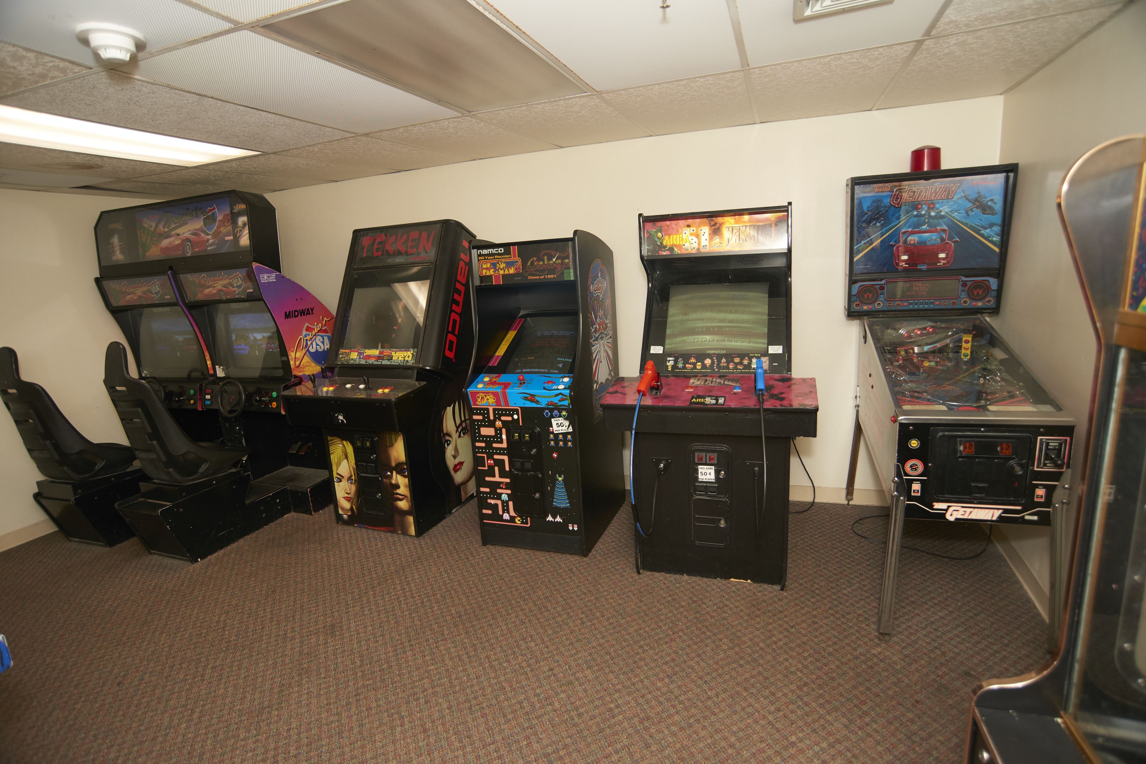 Una hilera de máquinas de arcade en una sala con pisos alfombrados y paredes lisas.