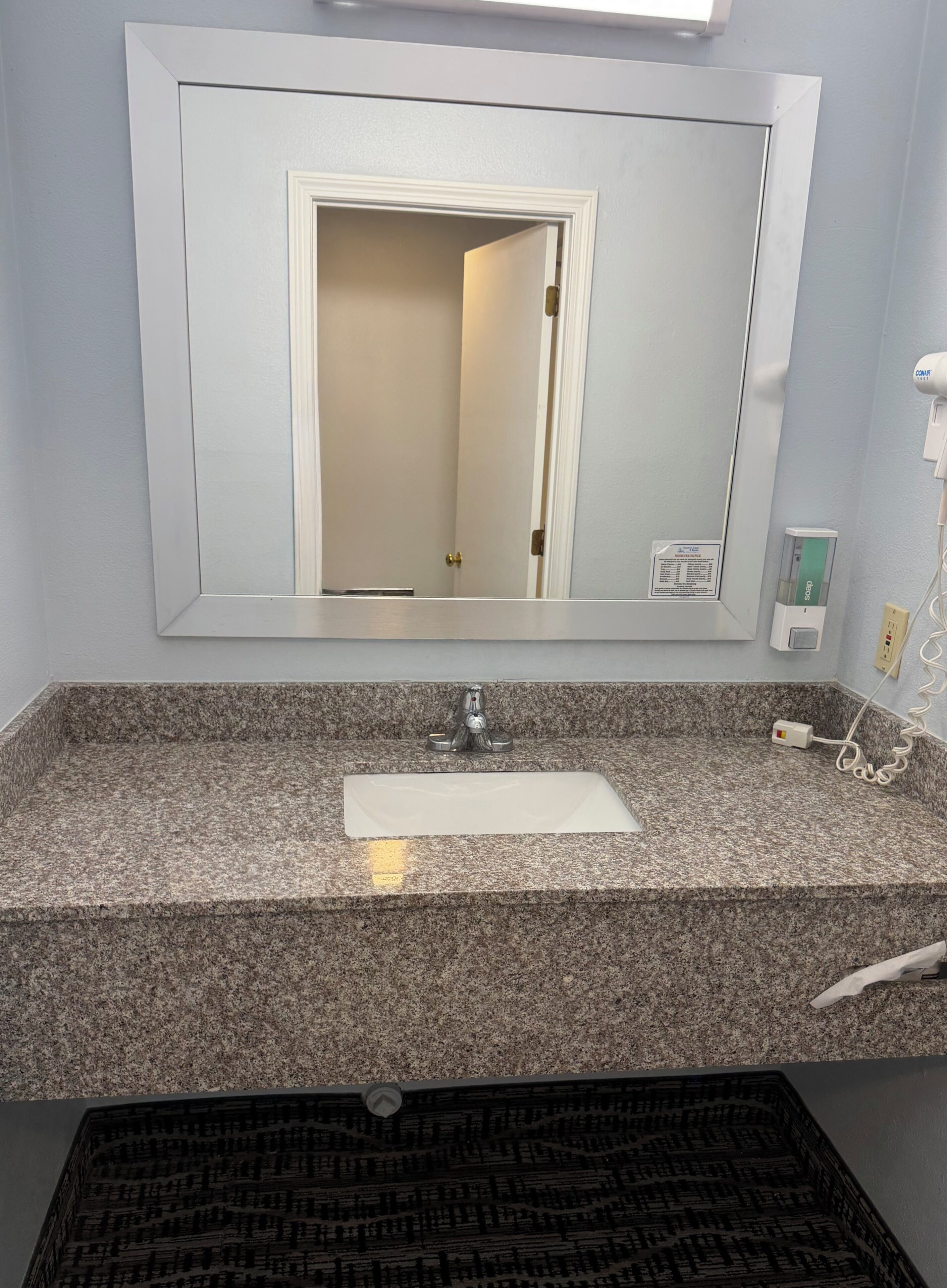 Un bany amb taulell de granit, un lavabo blanc, un mirall i una porta que dona a una altra estança.