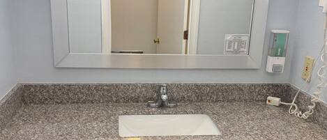 Un bany amb taulell de granit, un lavabo blanc, un mirall i una porta que dona a una altra estança.