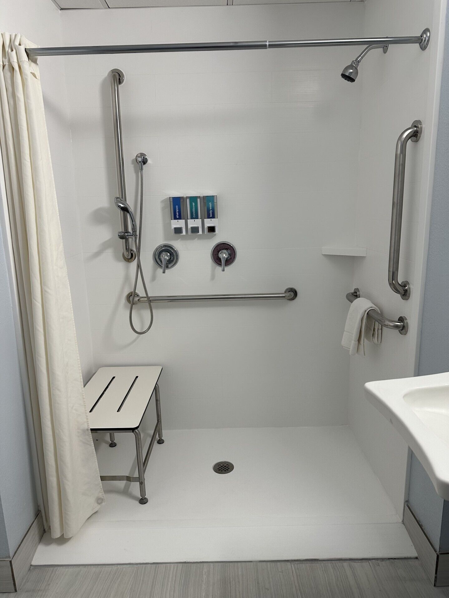 A modern bathroom with a walk-in shower, grab bars, a small vanity table, and a toilet with a safety grab bar.