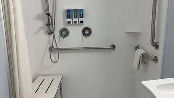 A modern bathroom with a walk-in shower, grab bars, a small vanity table, and a toilet with a safety grab bar.