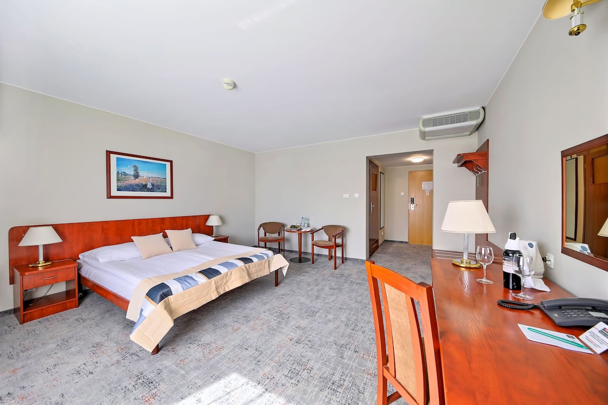 A hotel room with a bed, bedside table, lamp, desk with a chair, and a small table with chairs.