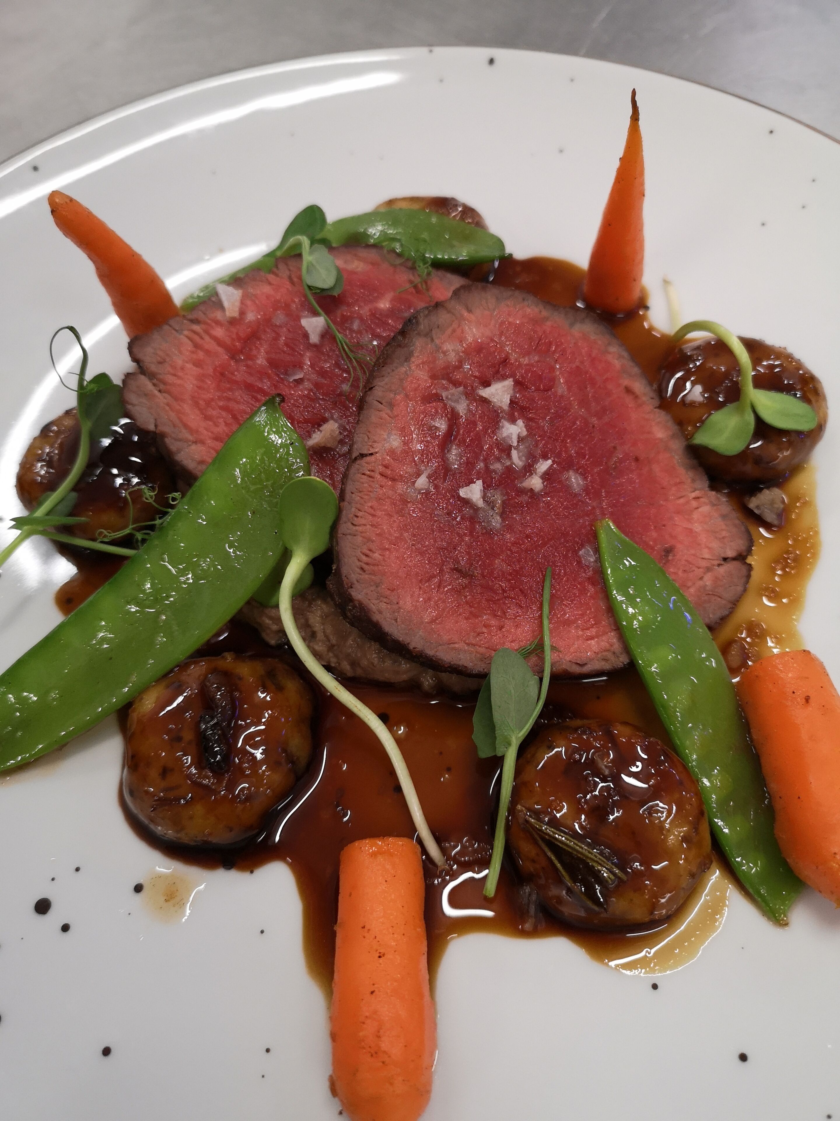 A plate of food with sliced meat, vegetables, and sauce.