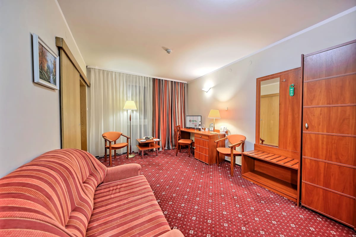A hotel room with a striped sofa, a desk with two chairs, a wardrobe, and a bed.