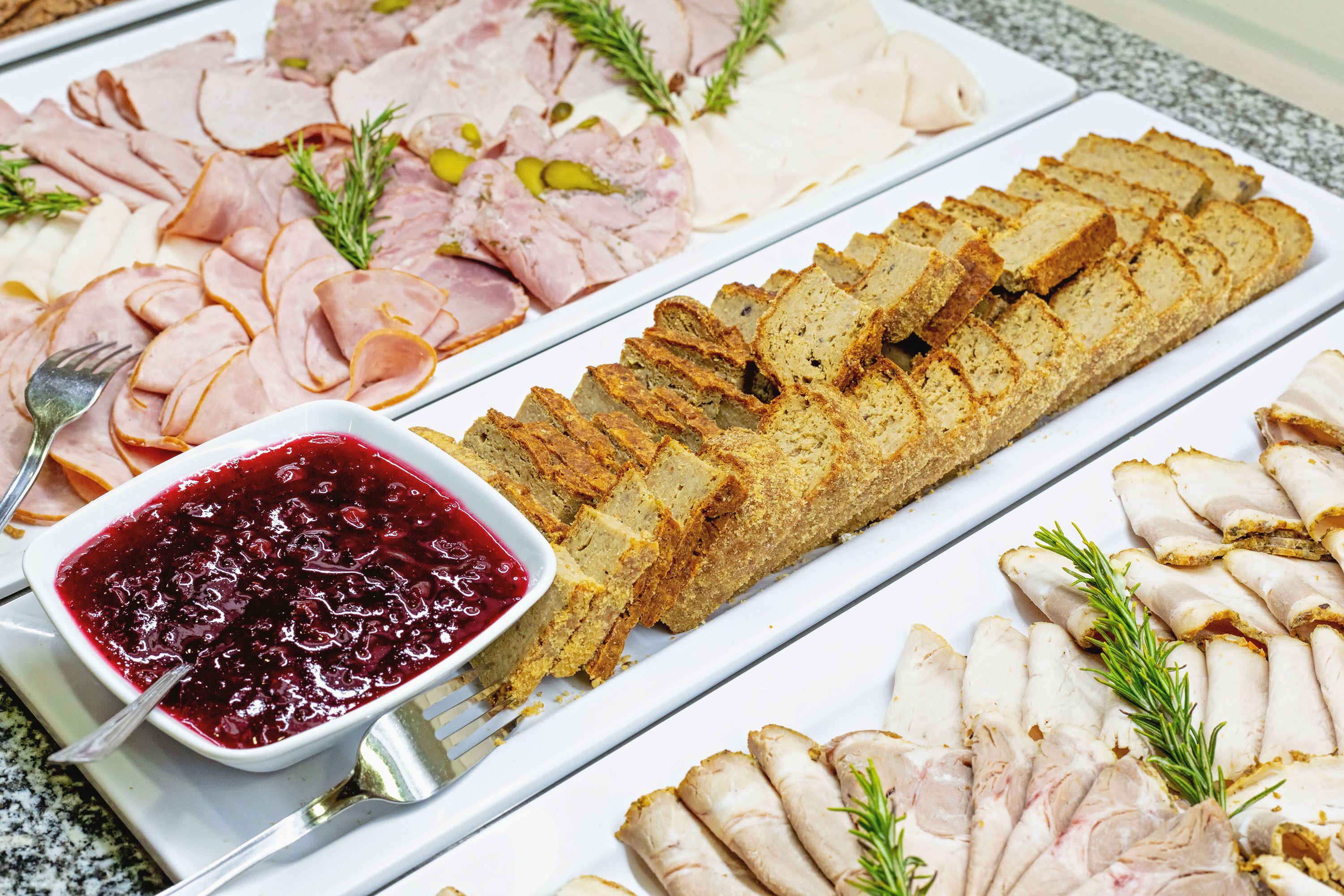 A charcuterie board with various meats, bread, and a bowl of cranberry sauce.