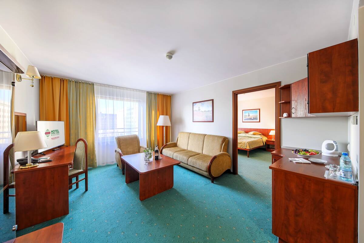 A hotel room with a desk, two chairs, a sofa, a bed, and a bathroom visible through an open door.