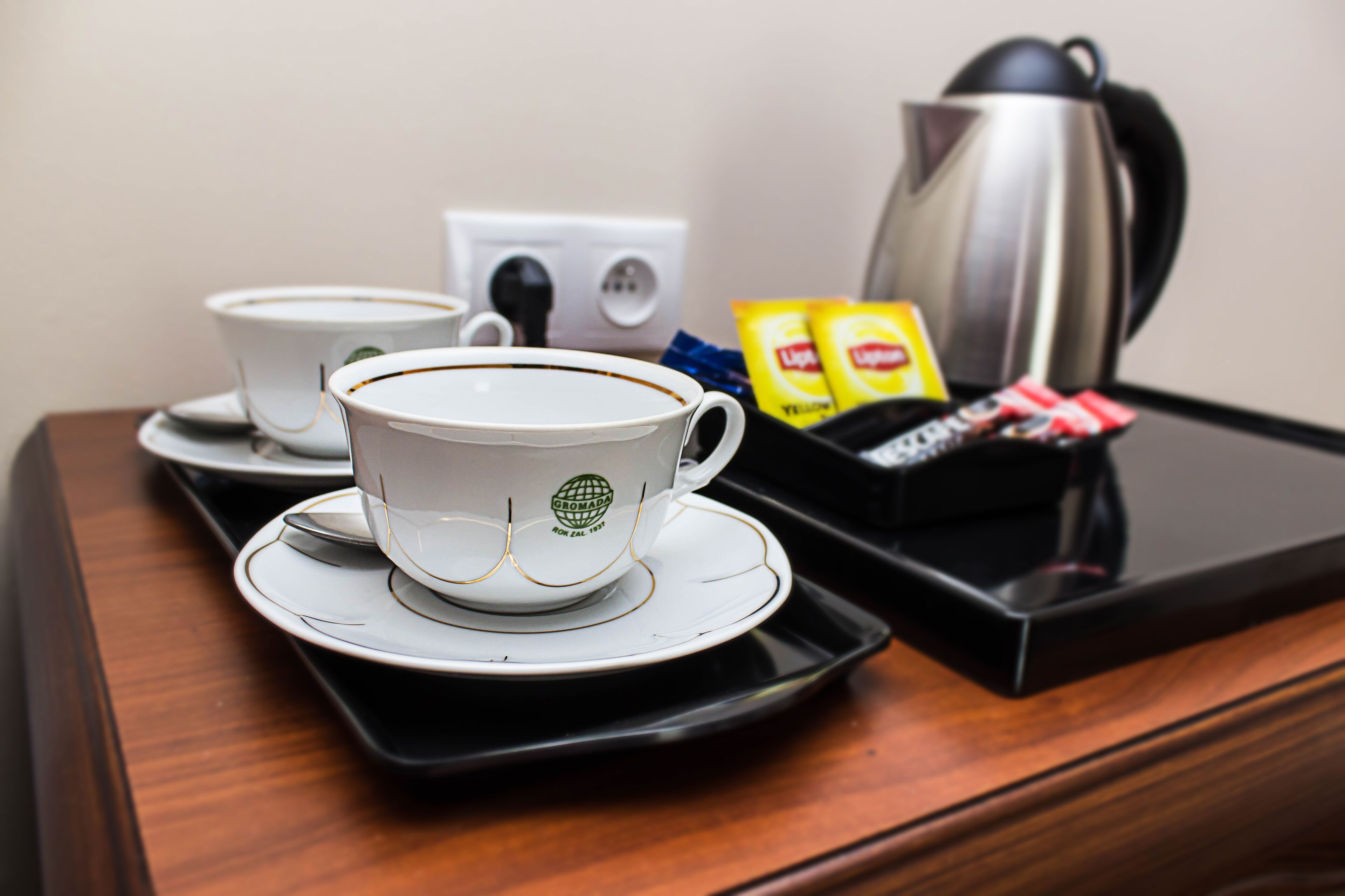 A tray with a coffee cup and saucer, a kettle, and some packets on a wooden surface.