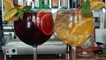 Two cocktails on a bar counter with a variety of liquor bottles in the background.