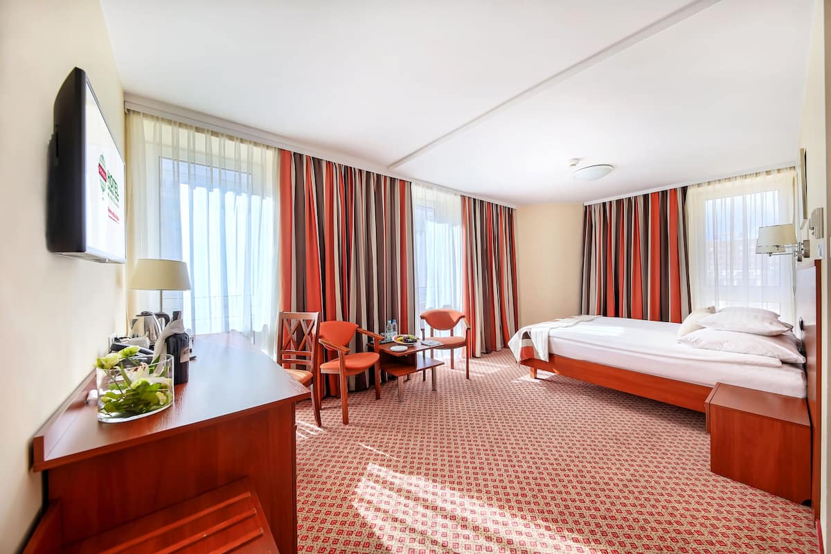 A hotel room with a bed, desk, chairs, and a small table.