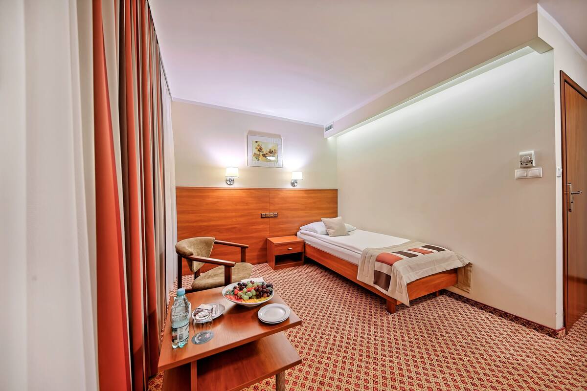 A hotel room with a bed, a desk with a plate of fruit, a chair, and a bedside table.