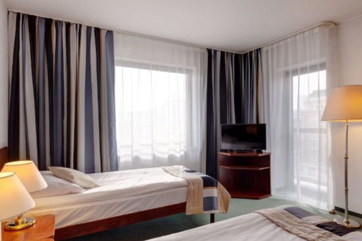A hotel room with two beds, a television, a desk with a lamp, and a large window with curtains.