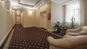 A hotel hallway with a patterned carpet, beige walls, and a potted plant by the window. - Hotel Hetman (Warsaw)