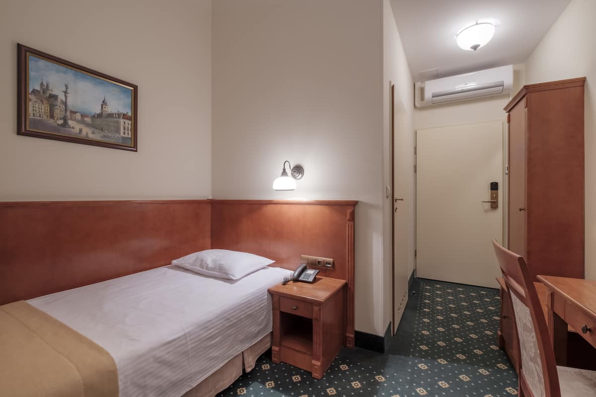 A hotel room with a single bed, a bedside table with a lamp, a telephone, and a painting on the wall.