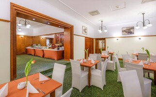 Uma área de refeições de hotel com mesas preparadas para o serviço, um buffet ao fundo e piso coberto por um tapete verde.