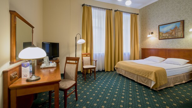A hotel room with a bed, desk, chairs, a television, and a painting on the wall. - Hotel Hetman (Warsaw)