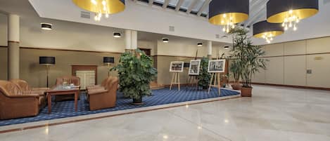 A spacious lobby with leather sofas, a coffee table, potted plants, easels with paintings, and modern pendant lighting.