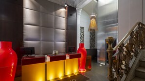 A reception desk with a modern design, a staircase with ornate railings, and a decorative hanging light fixture.
