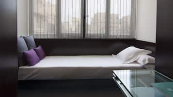 Una habitación pequeña y moderna con una cama individual, una mesita de vidrio y vistas a través de cortinas traslúcidas.