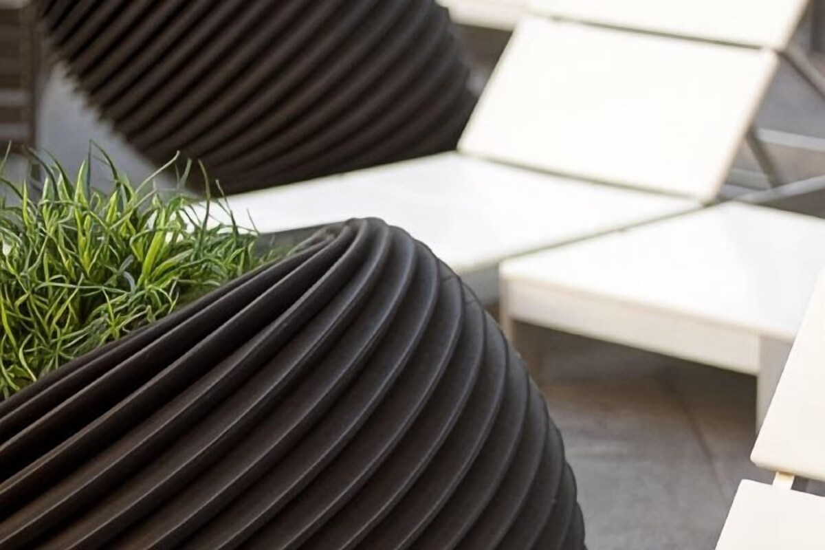 A modern outdoor seating area with black, ribbed planters and white lounge chairs.