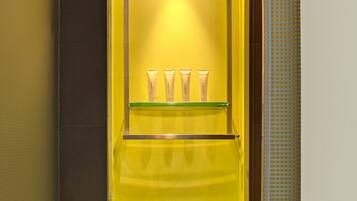 Un baño con cabina de vidrio amarillo, una repisa con artículos de aseo y una toalla.