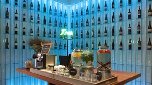 A bar area with a wall of wine bottles, a neon sign, and a variety of bar tools and glasses.
