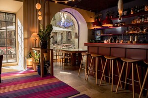 A bar area with stools, a bar counter, and shelves with bottles.