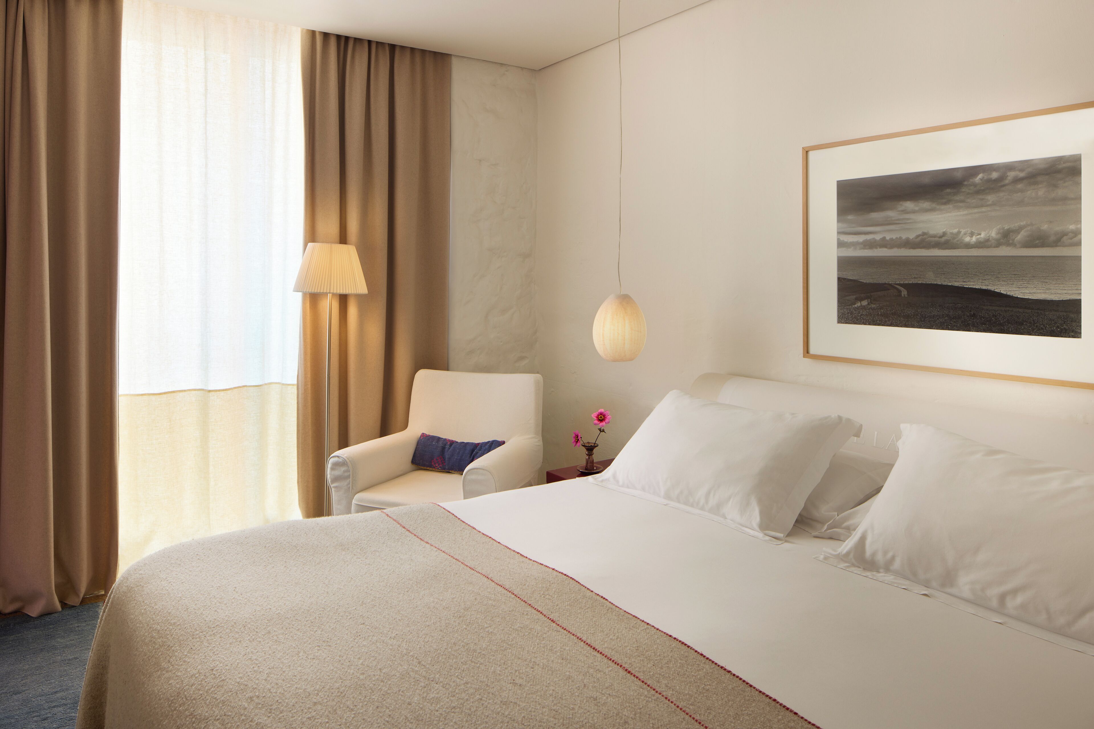 A hotel room with a bed, a chair, a lamp, and a framed picture on the wall.